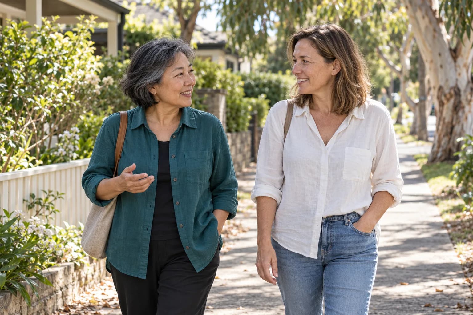 Two women talking as they walk along a leafy neighbourhood street.
